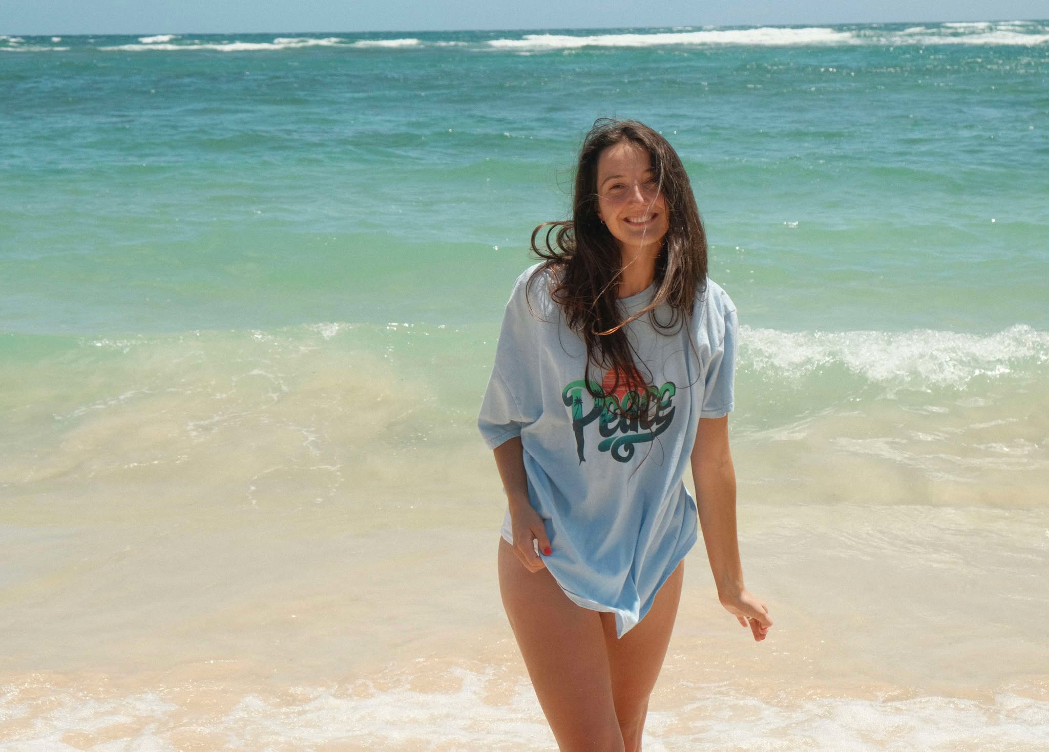 Woman standing on a beach with clear blue water and waves.